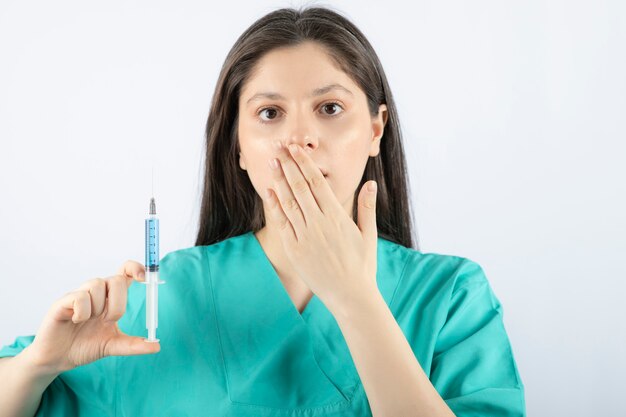 Portrait of female doctor holding a large syringe. 