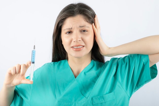 Portrait of female doctor holding a large syringe. 