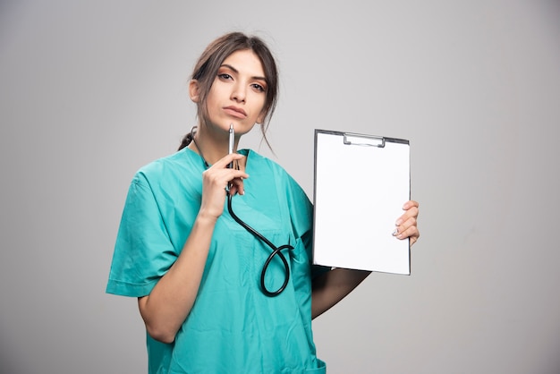 Portrait of female doctor posing with clipboard on gray