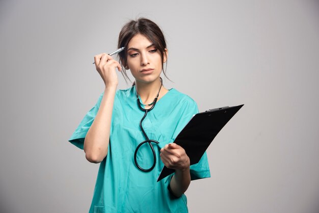 회색에 클립 보드와 함께 포즈를 취하는 여성 의사의 초상화