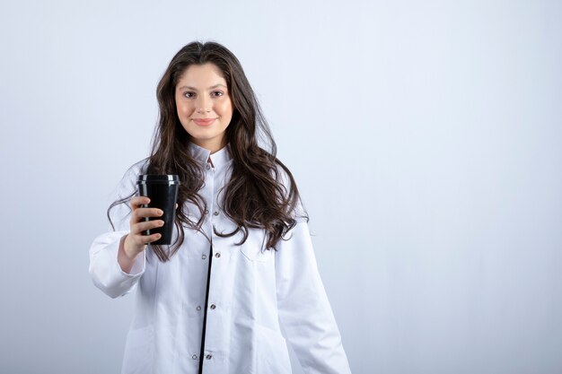 Portrait of female doctor posing with cup of coffee on grey. 