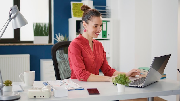 Portrait of female employee planning business strategy in startup office, using laptop to work with financial charts and sales statistics. Company accountant analyzing data research for growth.