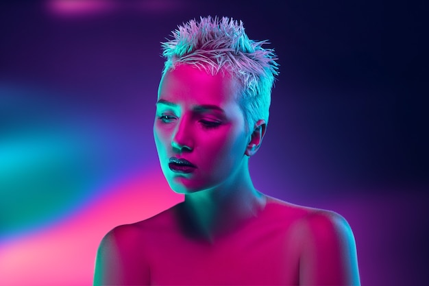 Portrait of female fashion model in neon light on dark studio background.