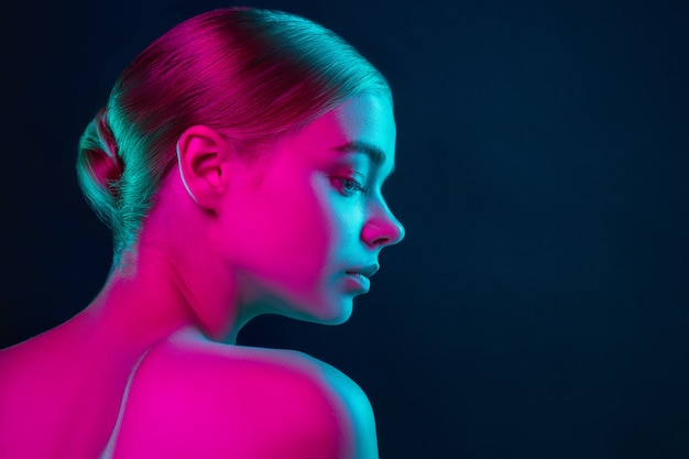 Portrait of female fashion model in neon light on dark studio