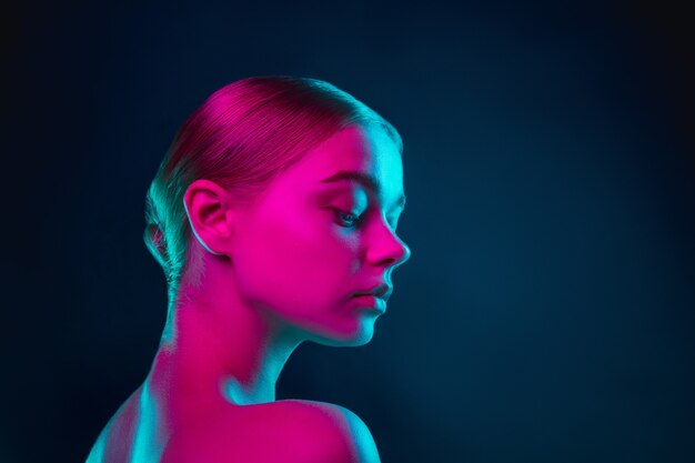 Portrait of female fashion model in neon light on dark studio