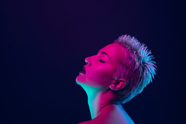 Portrait of female fashion model in neon light on dark studio.