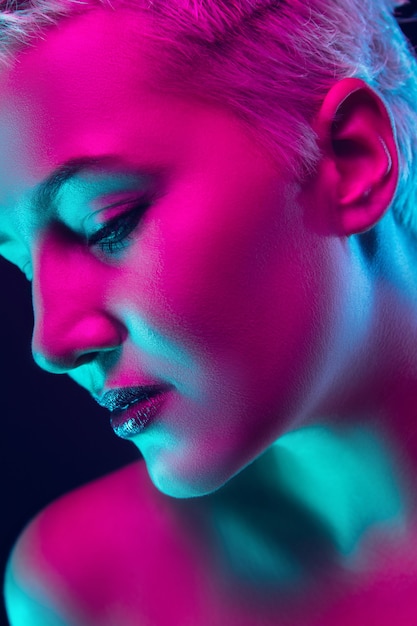 Portrait of female fashion model in neon light on dark studio.