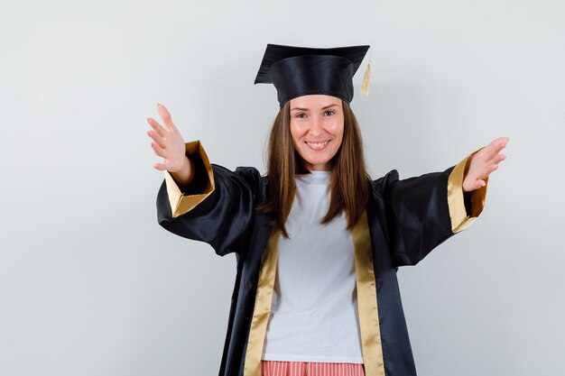 Portrait of female graduate opening arms for hug in uniform, casual clothes and looking happy front view