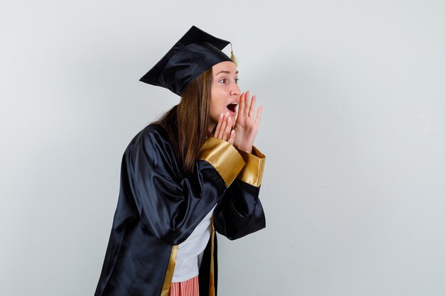 Portrait of female graduate shouting or announcing something in academic dress and looking excited front view