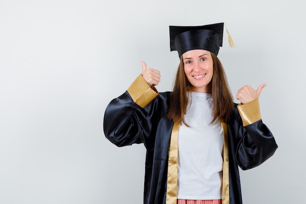 Portrait of female graduate showing double thumbs up in uniform, casual clothes and looking lucky front view