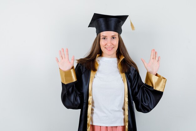 Portrait of female graduate showing palms in surrender gesture in uniform, casual clothes and looking confident front view