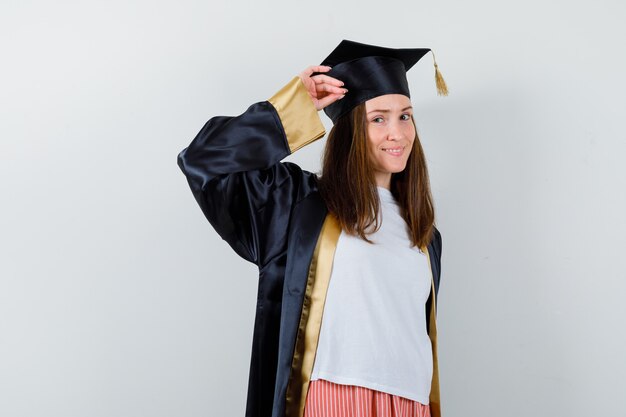 Portrait of female graduate showing salute gesture in uniform, casual clothes and looking confident front view