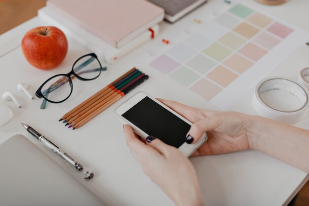 portrait of female hands with phone, apple, glasses, scotch and other stationery on white.