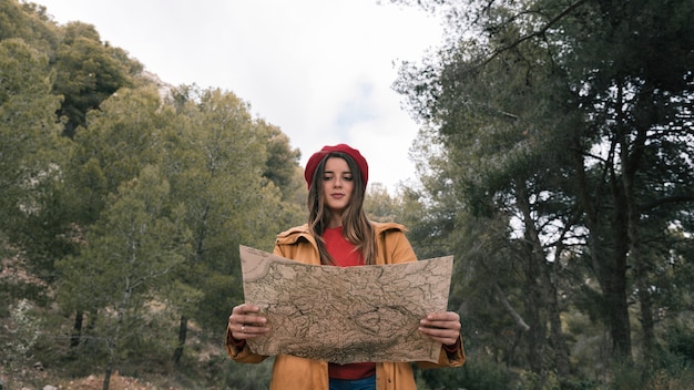 Foto gratuita ritratto di una viandante femmina in piedi nella foresta leggendo la mappa