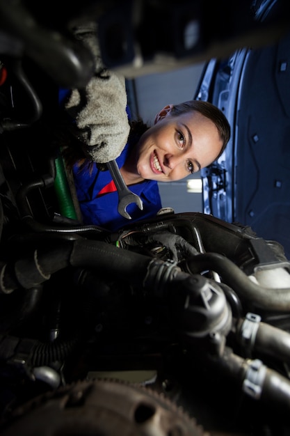 Portrait of female mechanic examining car engine