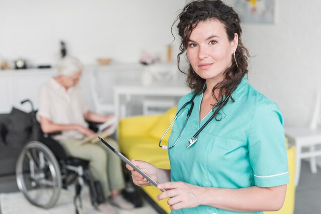 Портрет женщины медсестра, проведение цифровой планшет, стоя перед старший пациент на инвалидной коляске