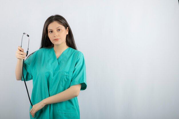 Portrait of female nurse holding stethoscope on white. 