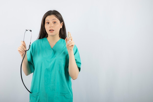 Portrait of female nurse holding stethoscope on white. 