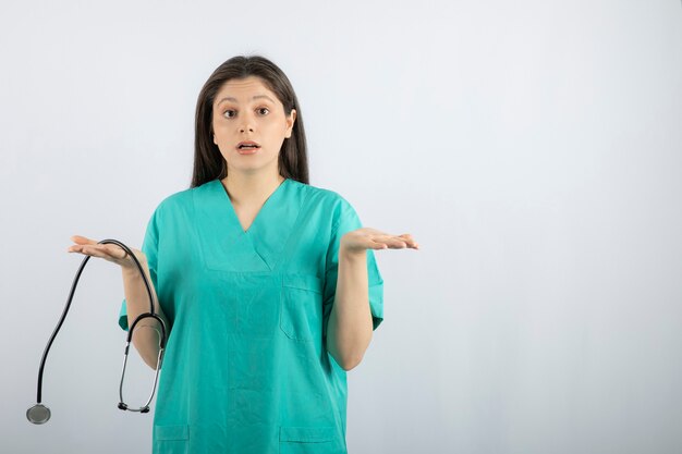 Portrait of female nurse with stethoscope having doubts on white. 