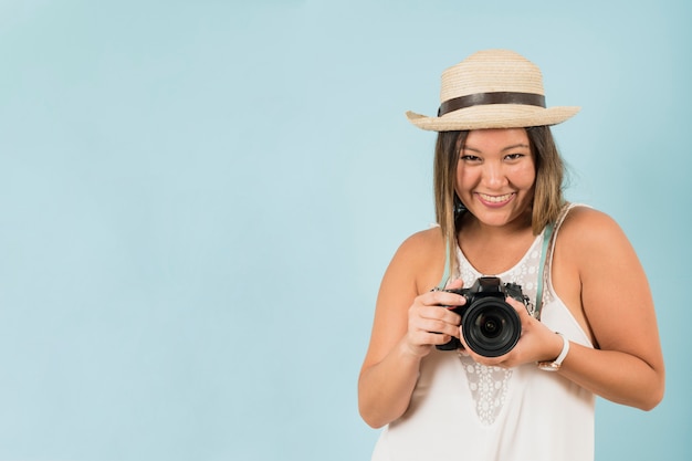 青い背景に対して彼女のプロのカメラでポーズをとって女性写真家の肖像画