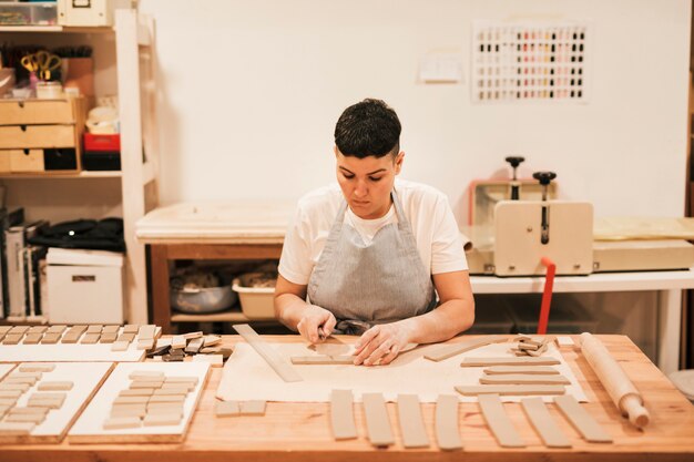 Portrait of female potter cutting the clay in rectangular shape on wooden table