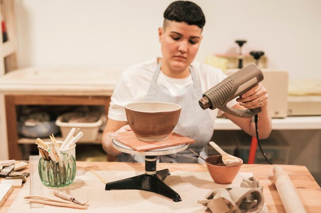 Portrait of a female potter drying the paint with dryer in the workshop