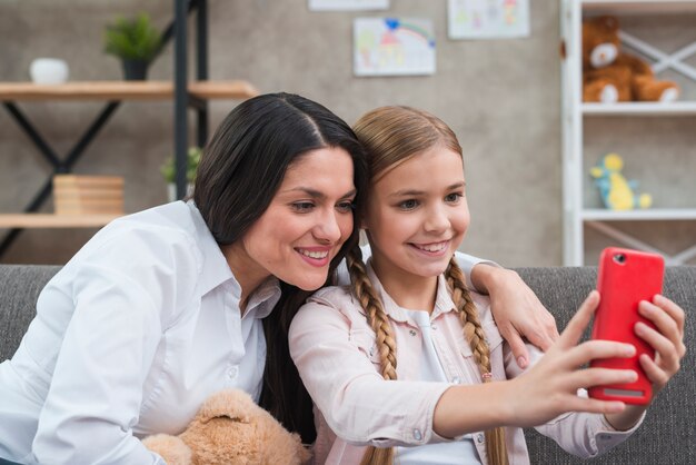 Portrait of female psychologist and girl taking selfie from mobile phone