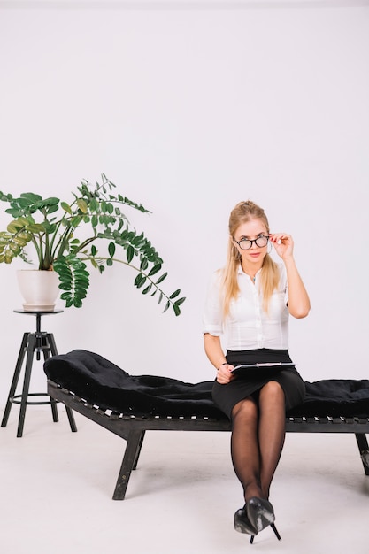 Free photo portrait of female psychologist sitting on couch holding clipboard in hand looking through eyeglasses