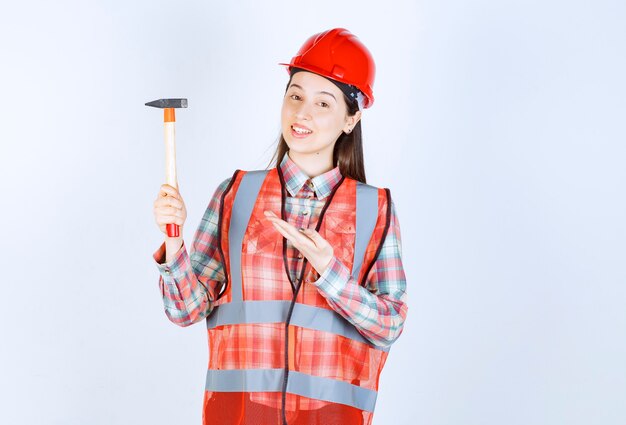 Portrait of female repairer in uniform standing with hammer over white wall. 