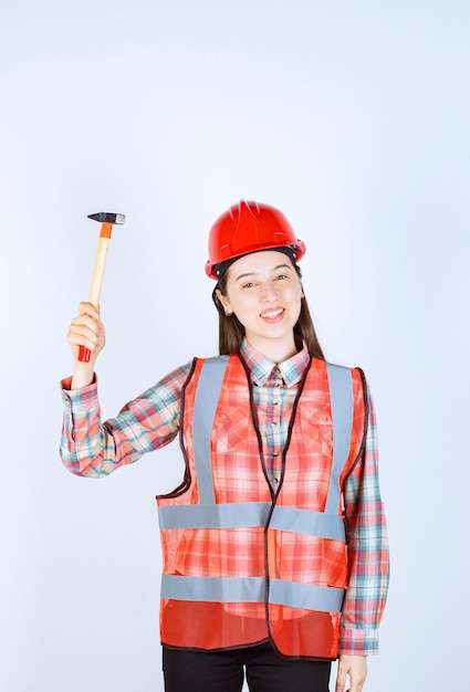 Portrait of female repairer in uniform standing with hammer over white wall. 