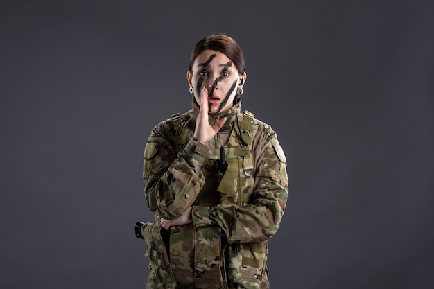 Portrait of female soldier in camouflage on dark wall