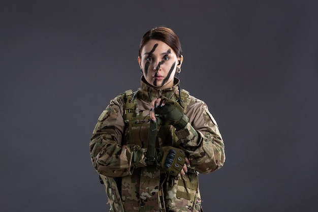 Portrait of female soldier in camouflage wearing gloves on dark wall