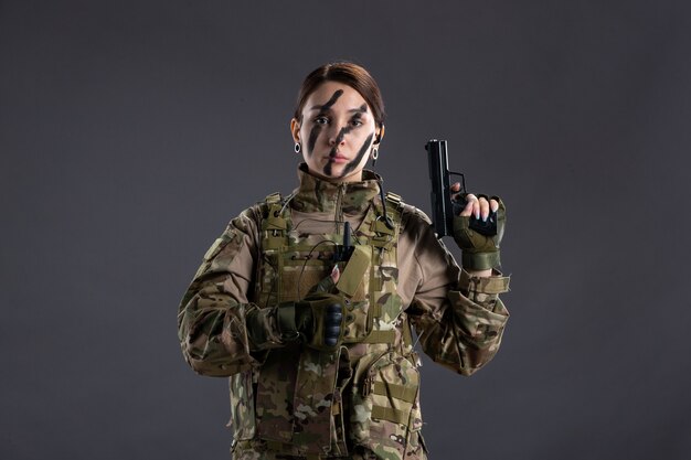 Portrait of female soldier in camouflage with gun on dark wall