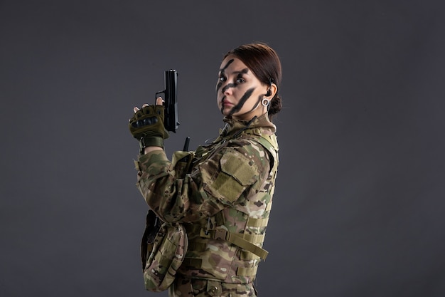 銃の暗い壁とカモフラージュの女性兵士の肖像画