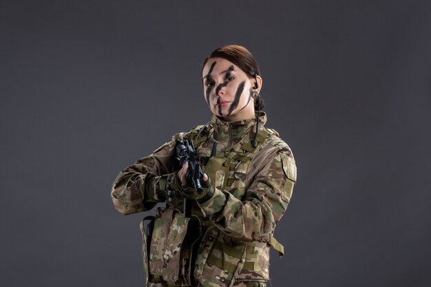 Портрет женщины-солдата в камуфляже с пулеметом на темной стене