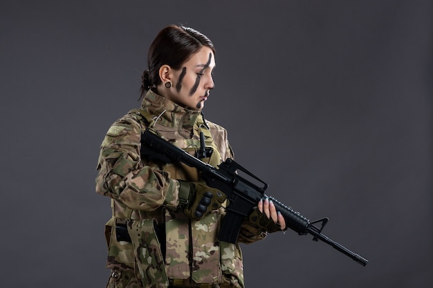 Free photo portrait of female soldier in camouflage with machine gun on dark wall