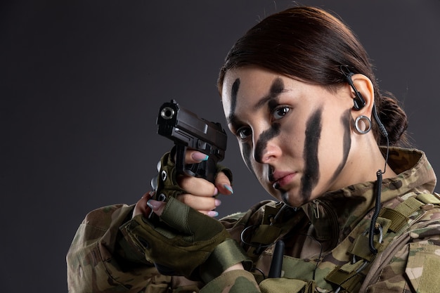 Portrait of female soldier in military uniform with gun on a dark wall