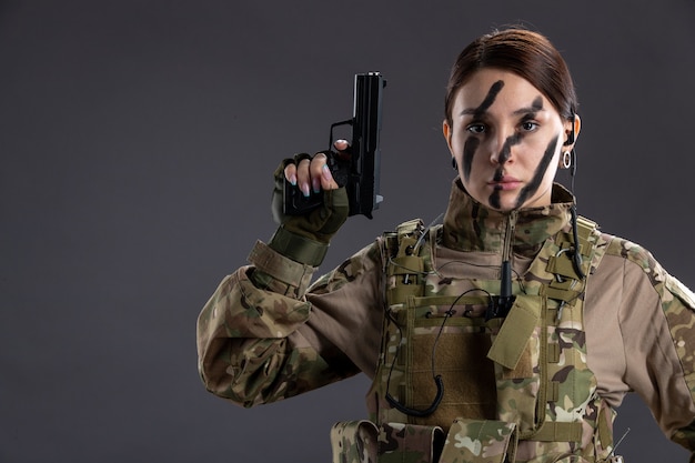Portrait of female soldier in military uniform with gun on dark wall