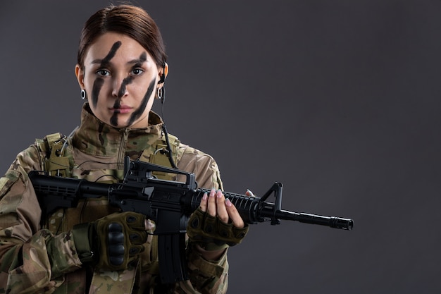 Portrait of female soldier in military uniform with machine gun on dark wall