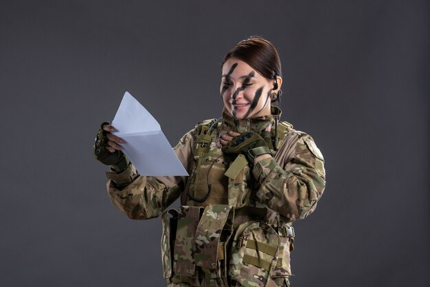 Portrait of female soldier reading letter on a dark wall