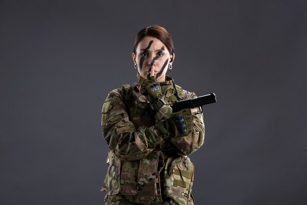 Portrait of female soldier with gun in camouflage dark wall