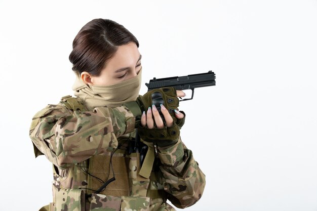 Portrait of female soldier with gun in camouflage white wall