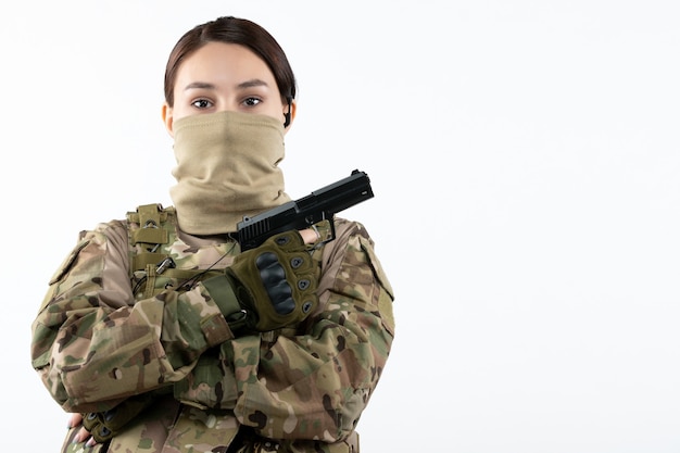 Portrait of female soldier with gun in camouflage white wall