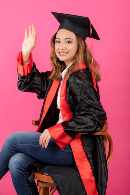 Portrait of female student wearing graduation gown shaking her hand