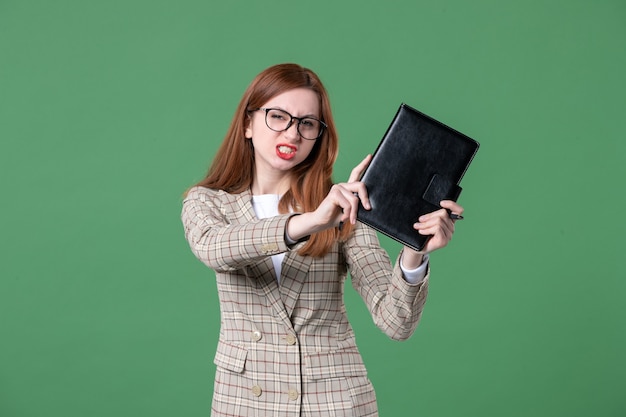 Portrait of female teacher angrily holding notepad on green