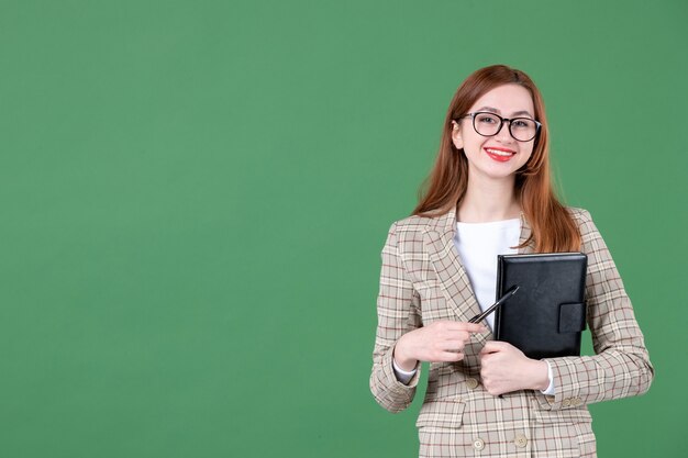 Portrait of female teacher holding notepad on green