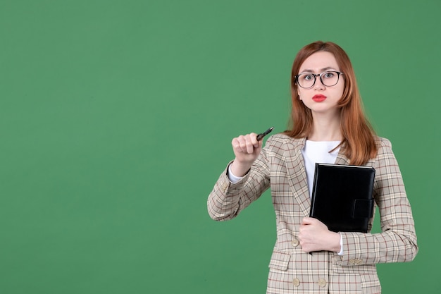 Portrait of female teacher holding notepad on green