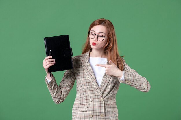 Portrait of female teacher holding notepad on green