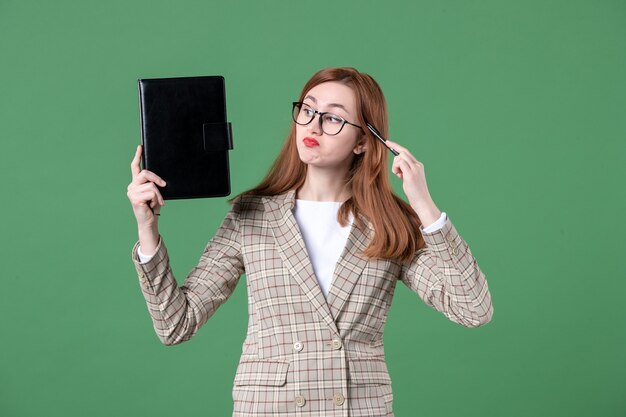 Portrait of female teacher holding notepad on green