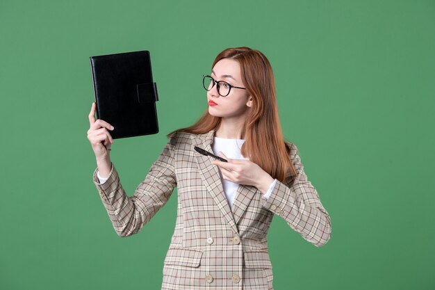 Portrait of female teacher holding notepad on green